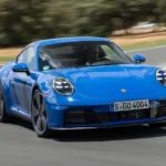 Porsche 911 Carrera 2025 azul em alta velocidade contornando uma curva em uma pista.